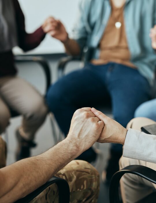 Close-up of group therapy attenders holding hands while sitting in a circle.